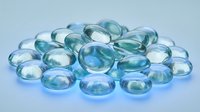Collection of translucent blue and green glass marbles scattered on white background for decorative crafts and gaming applications.