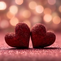 Two red glittery hearts touching on sparkling surface with warm bokeh lights background for Valentine's Day romance celebration and love concepts.