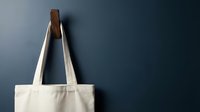 Blank white canvas tote bag hanging on a wooden hook against a dark blue wall, mockup with copy space for branding.