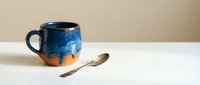 Handcrafted ceramic mug with blue glaze drip effect on terracotta base, artisan pottery for coffee tea drinking, rustic kitchen tableware home decor.
