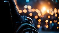 Silhouette of person in wheelchair against blurred city lights background creating atmospheric evening mood with warm bokeh effect and urban glow.