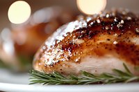 Juicy grilled chicken breast with crispy caramelized skin, seasoned with black pepper and fresh rosemary sprig on white plate, macro food photography with bokeh.
