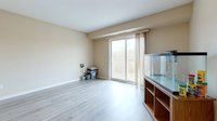 Bright empty living room with light wood flooring, beige walls, glass doors, and wooden aquarium cabinet with supplies for home interior design and real estate projects.