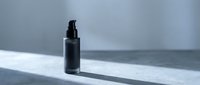 Black cosmetic pump bottle on white marble surface with dramatic lighting and shadows for skincare product packaging design.