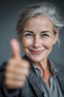 Confident mature businesswoman with gray hair giving thumbs up gesture, smiling at camera. Professional success and positive attitude concept.