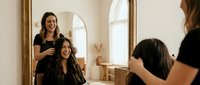 Professional hairstylist working on client's hair in modern salon with natural lighting and elegant interior design for beauty services.