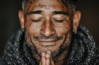 Peaceful middle-aged man with closed eyes and prayer hands showing gratitude, meditation and spiritual connection in warm natural lighting.