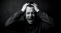 Stressed businessman holding head in hands screaming with intense emotional pain against dark background. Mental health and workplace pressure concept.