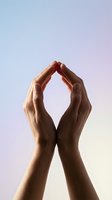 Two hands forming protective shelter gesture against soft gradient sky background symbolizing care, security and support concepts.