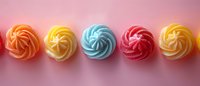 Colorful meringue cookies in swirl pattern arranged in row on pink background. Sweet pastel desserts with orange, yellow, blue, red, and yellow colors.