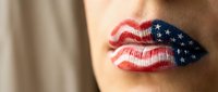Close-up of woman's lips painted with American flag design featuring red white blue stripes and stars for patriotic makeup concept.