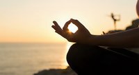 Silhouette of woman practicing yoga meditation at sunset beach with hands in mudra position creating peaceful mindfulness moment for wellness and relaxation.