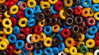 Colorful round cereal rings in vibrant blue, red, yellow and chocolate brown colors arranged in full frame pattern background. Close up view of breakfast food texture.