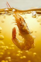 Fresh shrimp falling into golden cooking oil with bubbles, dramatic food photography perfect for restaurant menus, cookbooks and culinary advertising campaigns.
