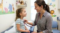 Female pediatrician examining young girl with stethoscope in colorful medical office. Healthcare professional conducting routine checkup on child patient.