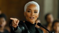 Confident African American woman with short platinum blonde hair speaking at microphone podium, gesturing with pointed finger during public presentation.