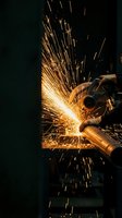 Industrial metalworking with angle grinder creating bright orange sparks flying in workshop. Professional manufacturing and fabrication process.
