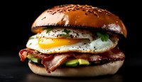 Gourmet breakfast burger with sunny side up egg, crispy bacon, fresh avocado slices and herbs on brioche bun against dark background. Perfect for menu design.