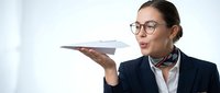 Young Asian woman in business attire wearing glasses holds paper airplane, representing innovation, creativity, and forward-thinking entrepreneurship for corporate projects.
