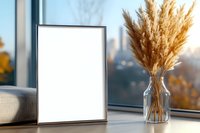 Empty silver frame mockup with pampas grass bouquet in glass vase on windowsill against blurred autumn cityscape background. Modern minimal home decor.