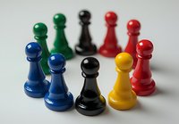 Colorful chess pawns arranged in curved formation on white surface showing leadership and teamwork concept, featuring blue, black, red, and yellow pieces.