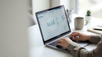 Business professional analyzing financial data and charts on laptop computer in modern office workspace for corporate reporting and analytics.