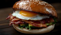 Appetizing breakfast burger with crispy bacon strips, sunny side up egg, and fresh lettuce on toasted sesame bun, served on rustic wooden surface.