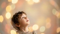 Young curly-haired boy looking up with wonder and curiosity against warm bokeh lights background, expressing hope, dreams and childhood imagination.