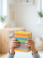 Child holding stack of colorful books with rainbow spine stripes in bright yellow, orange, blue, green, and pink for early literacy and education.