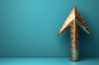 Golden glitter arrow pointing upward against turquoise background, symbolizing growth, success and positive business direction in minimal composition.