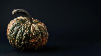 Textured ornamental gourd with green and gold striped ridges against dark background, suitable for autumn harvest and seasonal design projects.