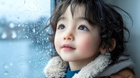 Young Asian girl with curly dark hair and rosy cheeks gazes dreamily through rainy window while wearing cozy sherpa collar jacket, capturing childhood wonder and innocence.