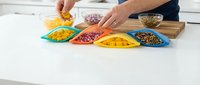 Person's hands adding ingredients to colorful bowls containing grains, legumes, and seeds on white kitchen counter for meal preparation and healthy cooking.
