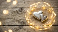 Two silver hearts surrounded by warm fairy lights on rustic wooden background for romantic decoration and wedding design projects.