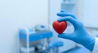 Medical professional in blue gloves holding red heart symbol in modern healthcare facility representing cardiology and patient care.