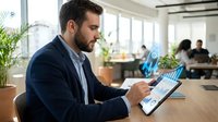 Professional businessman analyzing financial data on tablet with holographic charts in modern office workspace.