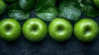 Fresh green apples with water drops arranged in row on dark background. Natural organic fruits with wet glossy surface create appetizing composition.