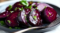 Fresh sliced beetroot garnished with herbs on dark plate, close up view showing vibrant purple color and moist texture. Healthy vegetarian food styling.