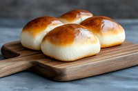 Fresh homemade milk bread rolls with golden brown crust served on wooden cutting board against gray concrete background, close up view of soft Japanese style buns.