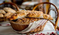 Fresh braided challah bread loaves in wicker basket on traditional embroidered cloth, warm golden crust with glossy finish, artisanal bakery setting.