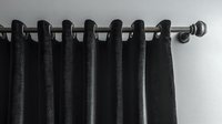 Black grommet curtain panel hanging on metal rod against white wall, creating elegant window treatment with clean lines and modern minimalist style.