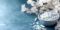 White homeopathic pills and spring cherry blossom branch on blue textured background with copy space, natural alternative medicine concept.