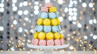 Colorful macaron tower with pastel pink, yellow and mint green French cookies stacked on white plate against sparkling bokeh lights background for celebrations.