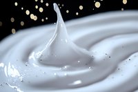 Swirling white cream splash with soft peak against dark background with golden bokeh lights creates elegant dairy product advertising composition.