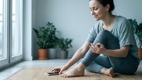 Young woman sitting on floor using smartphone in bright modern home interior with plants by window for lifestyle and technology concepts.