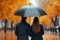 Couple sharing umbrella in rain, walking through autumn park with orange foliage. Romantic mood enhanced by soft bokeh and rainy atmosphere.