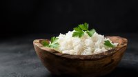 Cooked white rice in wooden bowl garnished with fresh parsley on dark background for culinary and food photography projects.