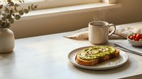 Avocado toast on a ceramic plate with steaming coffee mug, cherry tomatoes, and eucalyptus on a marble table in warm morning light.