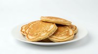Stack of golden pancakes served on white plate, ready for breakfast or brunch dining.