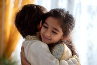 Young Hispanic girl with long dark hair embracing parent in warm sunlit room, expressing love and tenderness through genuine emotional connection and gentle smile.